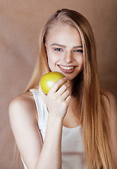 Image showing young pretty blond woman with green apple happy cheerful smiling close up on warm brown background, lifestyle people concept