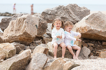 Image showing Children on the sea beach. Twins sitting against stones and sea water.