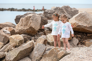 Image showing Children on the sea beach. Twins standing against stones and sea water.