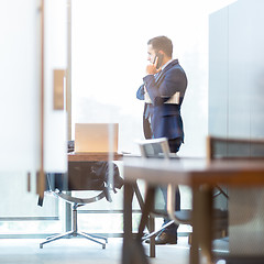 Image showing Businessman talking on a mobile phone while looking through window.