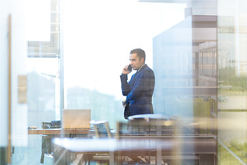 Image showing Businessman talking on a mobile phone while looking through office window.