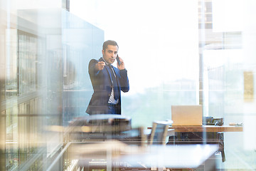 Image showing Businessman talking on a mobile phone in corporate office, pointing to camera.