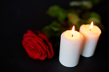 Image showing red rose and burning candles over black background