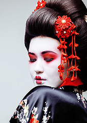 Image showing young pretty geisha in black kimono among sakura, asian ethno close up