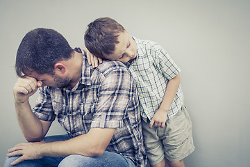 Image showing sad son hugging his dad near wall