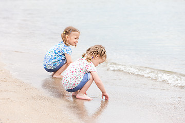 Image showing Children on the sea beach. Twins sitting along sea water.