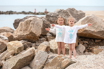 Image showing Children on the sea beach. Twins standing against stones and sea water.