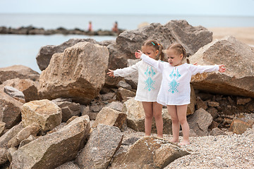 Image showing Children on the sea beach. Twins standing against stones and sea water.