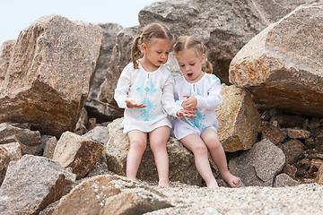 Image showing Children on the sea beach. Twins sitting against stones and sea water.