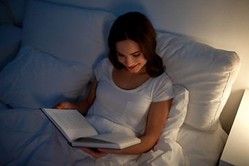 Image showing young woman reading book in bed at night home