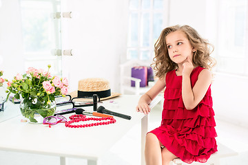 Image showing A little girl with cosmetics. She is in mother\'s bedroom, sitting near the mirror.