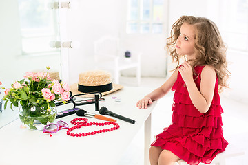 Image showing A little girl with cosmetics. She is in mother\'s bedroom, sitting near the mirror.