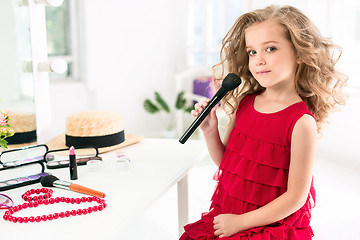 Image showing A little girl with cosmetics. She is in mother\'s bedroom, sitting near the mirror.