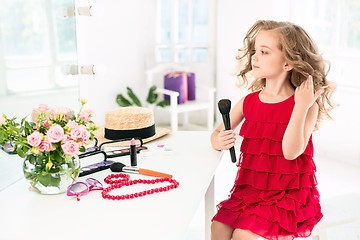 Image showing A little girl with cosmetics. She is in mother\'s bedroom, sitting near the mirror.