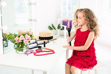 Image showing A little girl with cosmetics. She is in mother\'s bedroom, sitting near the mirror.