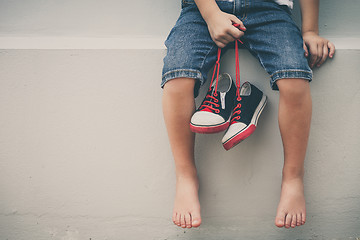 Image showing Little boy  sitting near the house and keeping the youth sneaker