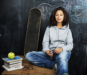 Image showing young cute teenage girl in classroom at blackboard seating on ta