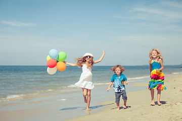 Image showing Three happy children with balloons  dancing on the beach