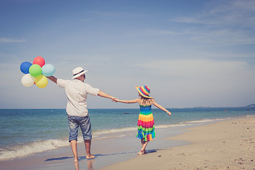 Image showing Father and daughter with balloons playing on the beach at the da