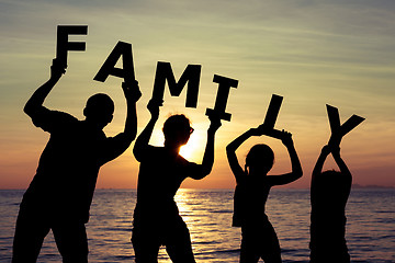 Image showing Happy family standing on the beach at the sunset time. 