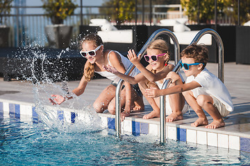 Image showing Three happy children sitting near swimming pool at the day time.