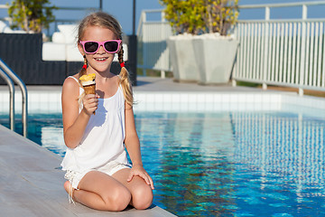 Image showing happy little girl with ice cream sitting near a swimming pool at