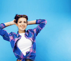 Image showing young pretty teenage modern hipster girl posing emotional happy smiling on blue background, lifestyle people concept 