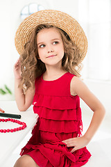 Image showing A little girl with cosmetics. She is in mother\'s bedroom, sitting near the mirror.