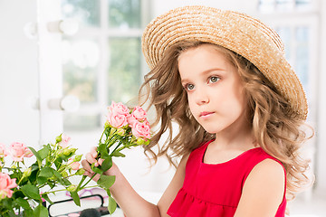 Image showing A little girl with roses. She is in mother\'s bedroom, sitting near the mirror.