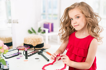 Image showing A little girl with cosmetics. She is in mother\'s bedroom, sitting near the mirror.