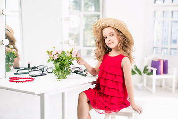 Image showing A little girl with cosmetics. She is in mother\'s bedroom, sitting near the mirror.