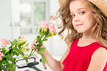 Image showing A little girl with roses. She is in mother\'s bedroom, sitting near the mirror.