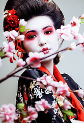 Image showing young pretty geisha in kimono with sakura and red decoration design on white background
