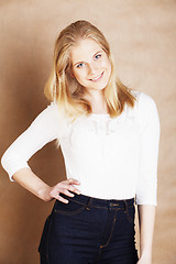 Image showing young cool blong teenage girl messed with her hair smiling close up on warm brown background, lifestyle people concept