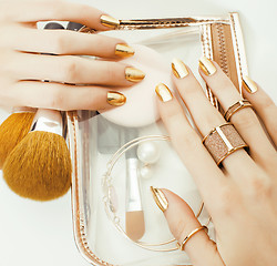 Image showing woman hands with golden manicure and many rings holding brushes, makeup artist stuff stylish, pure close up pink flower rose tenderness among cosmetic