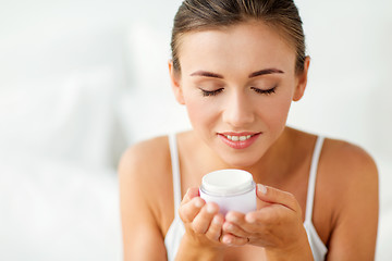 Image showing close up of happy woman holding and smelling cream