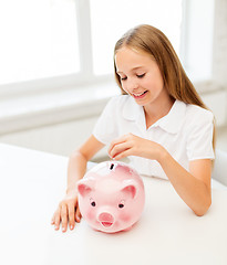 Image showing happy smiling girl putting coin into piggy bank