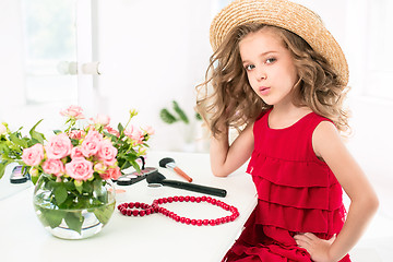 Image showing A little girl with cosmetics. She is in mother\'s bedroom, sitting near the mirror.