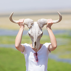 Image showing Woman holding a white wildebeest skull wearing it like a mask in nature on african wildlife safari.