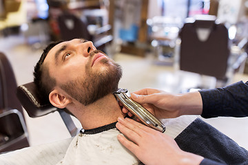 Image showing man and barber with trimmer cutting beard at salon