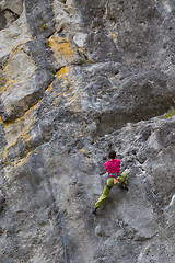 Image showing Strong girl climbs on a rock, doing sports climbing in nature.