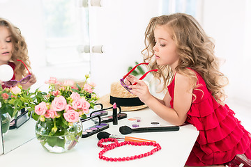 Image showing A little girl with cosmetics. She is in mother\'s bedroom, sitting near the mirror.