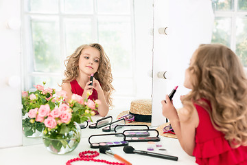 Image showing A little girl with cosmetics. She is in mother\'s bedroom, sitting near the mirror.