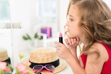 Image showing A little girl with cosmetics. She is in mother\'s bedroom, sitting near the mirror.