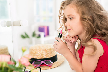 Image showing A little girl with cosmetics. She is in mother\'s bedroom, sitting near the mirror.