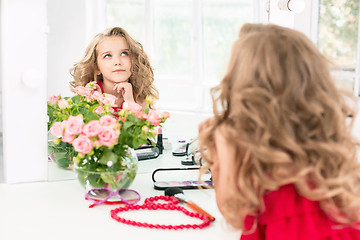 Image showing A little girl with cosmetics. She is in mother\'s bedroom, sitting near the mirror.