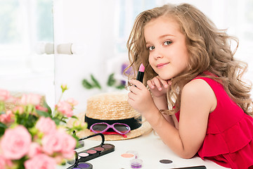 Image showing A little girl with cosmetics. She is in mother\'s bedroom, sitting near the mirror.