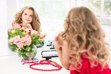 Image showing A little girl with cosmetics. She is in mother\'s bedroom, sitting near the mirror.