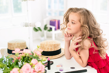 Image showing A little girl with cosmetics. She is in mother\'s bedroom, sitting near the mirror.