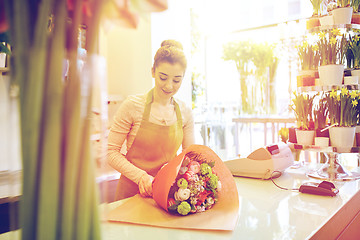 Image showing smiling florist woman packing bunch at flower shop